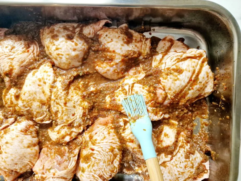 spreading jerk marinade over chicken thighs