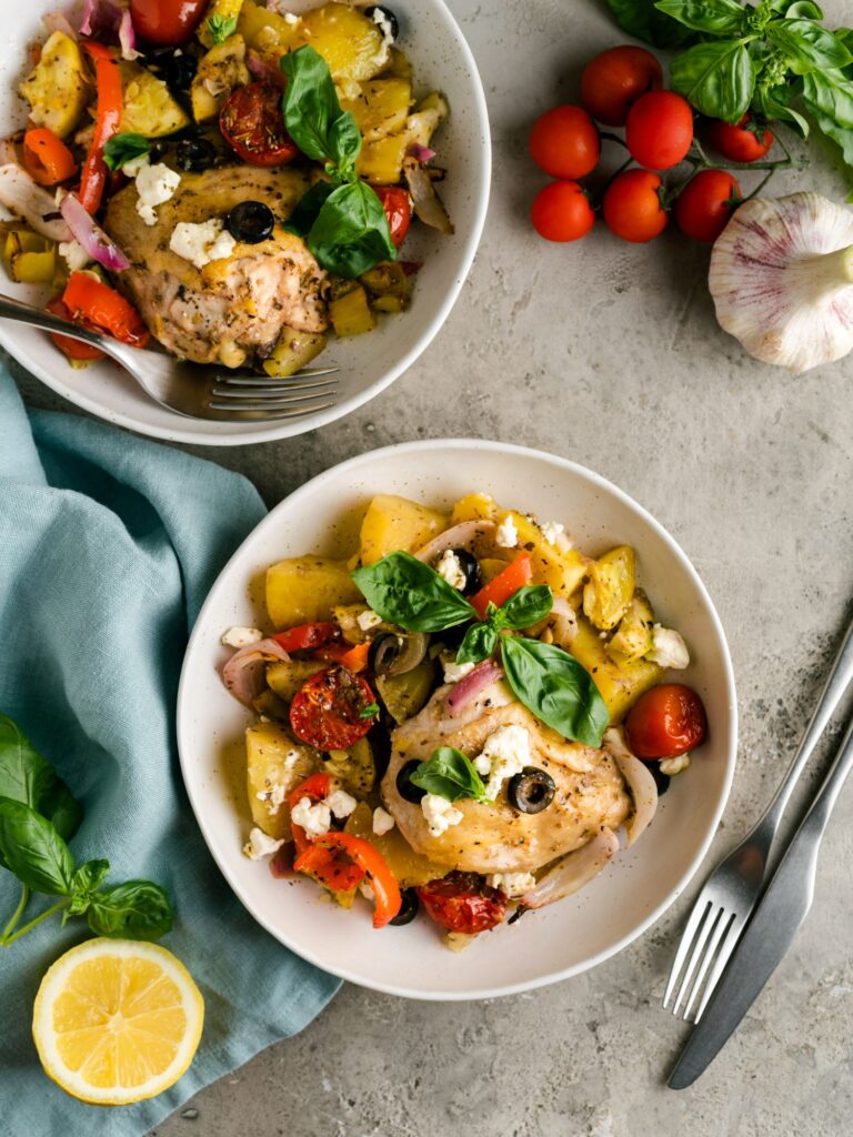 Mediterranean Chicken Tray Bake served in two bowls with fresh ingredients surrounding it