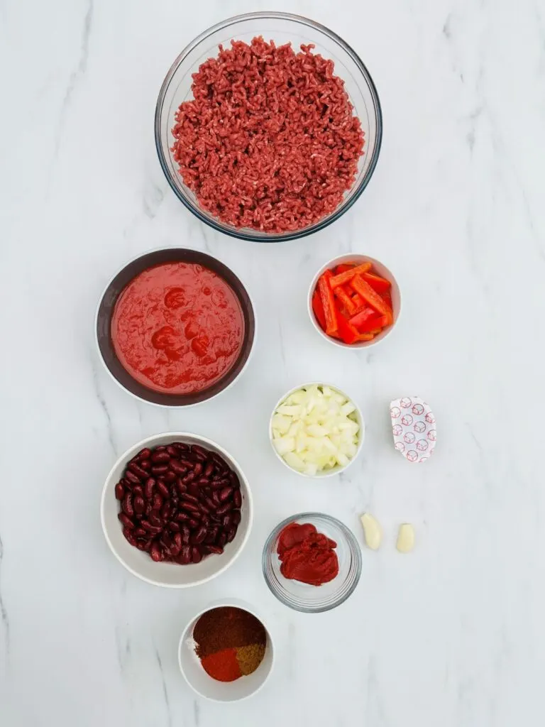 chilli con carne ingredients, mince, chopped tomatoes, sliced red peppers, chopped onions, beef stock pot, two cloves garlic, tomato puree, red kidney beans and spices