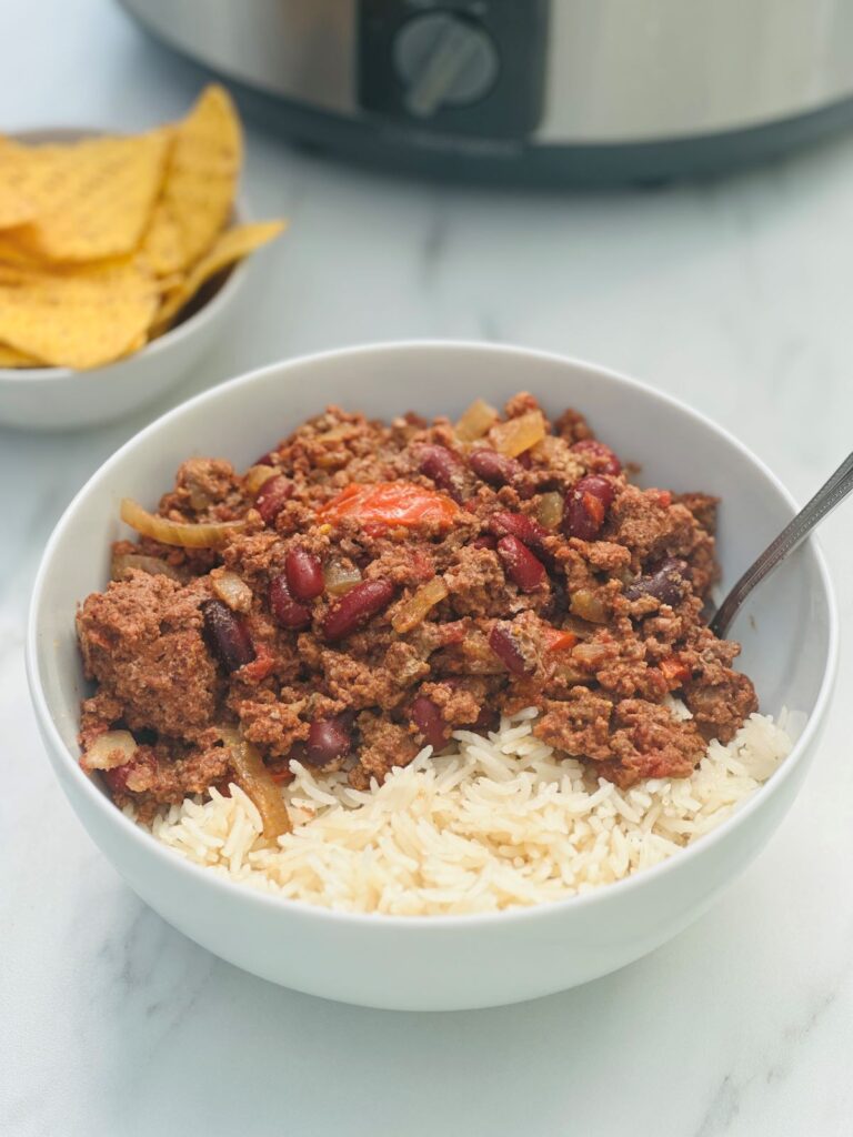 bowl of chilli con carne and rice next to some tortilla chips with slow cooker 
