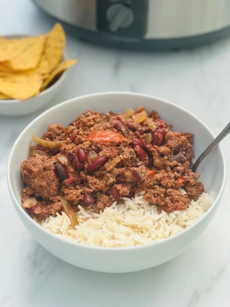 bowl of chilli con carne and rice next to some tortilla chips with slow cooker