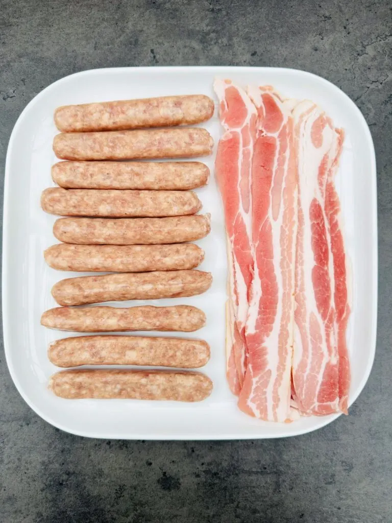 raw chipolatas and streaky bacon on a plate 