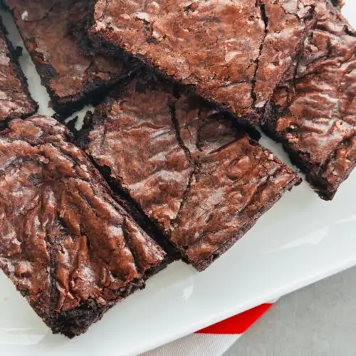 chocolate brownies sliced and on a white plate sitting on top of a red and white striped cloth