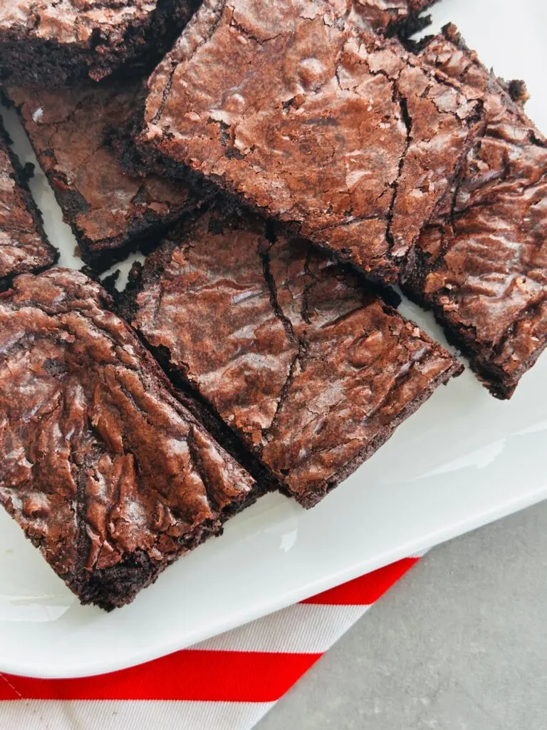 chocolate brownies sliced and on a white plate sitting on top of a red and white striped cloth