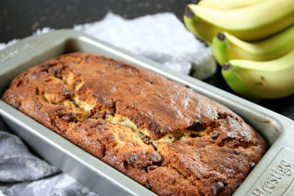banana bread with chocolate chips cooling down in loaf tin next to some bananas