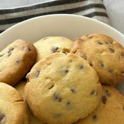 hocolate chip shortbread cookies piled in a white bowl on a striped cloth