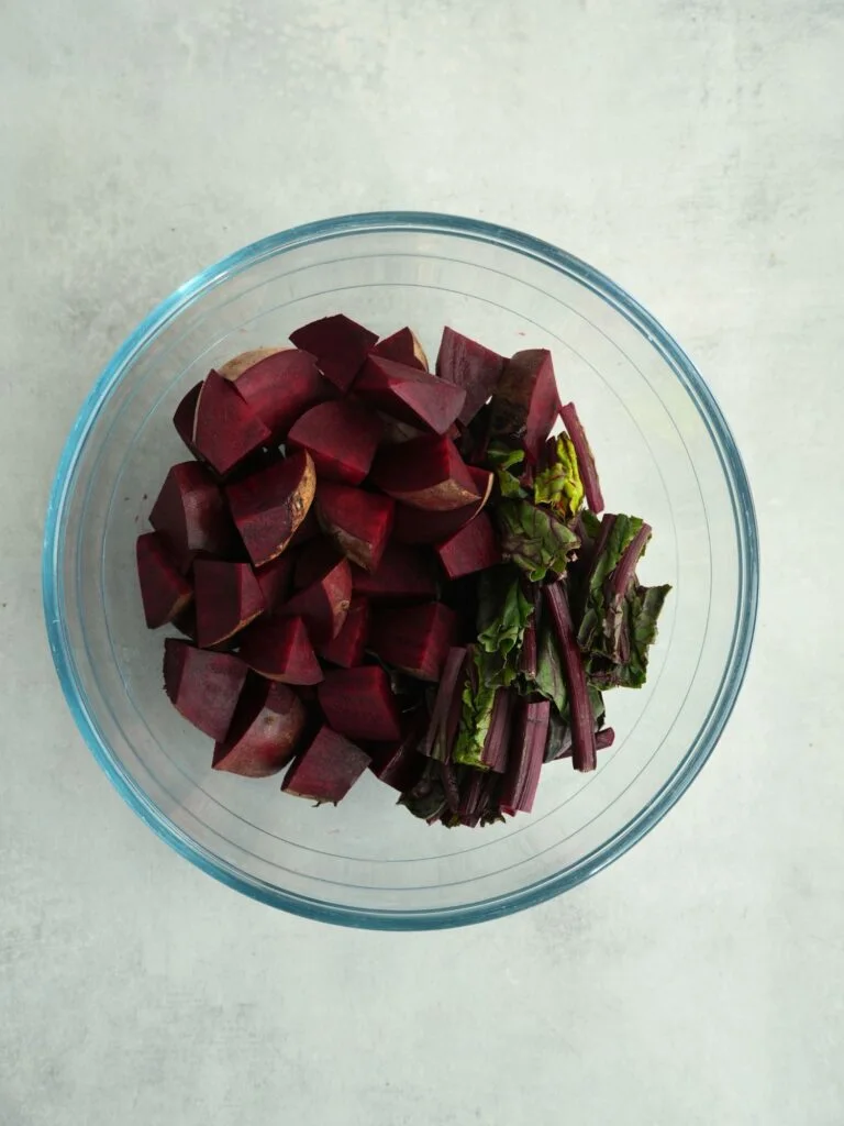 chopped raw beetroot with stalks, leaves and skin on in a glass bowl