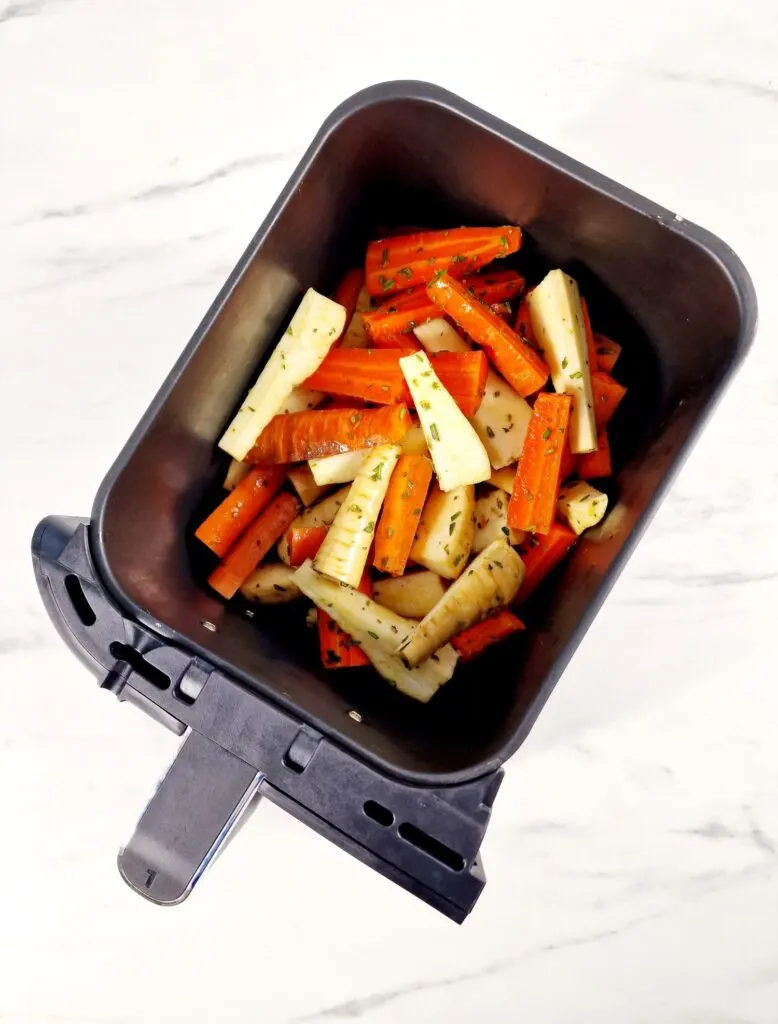 chopped carrots and parsnips in an air fryer basket with fresh chopped rosemary sprinkled on top