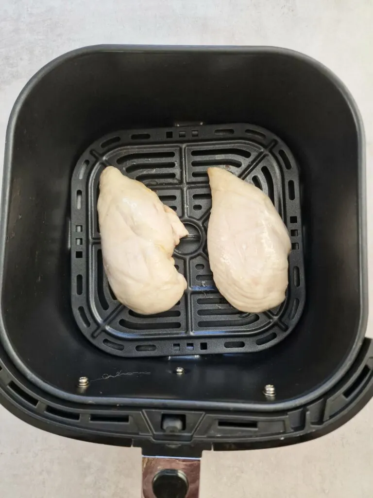 two cooked chicken breasts in air fryer basket