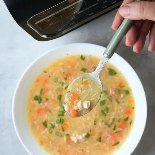 chicken and potato soup in a bowl with carrots and fresh parsley with a spoon held above it