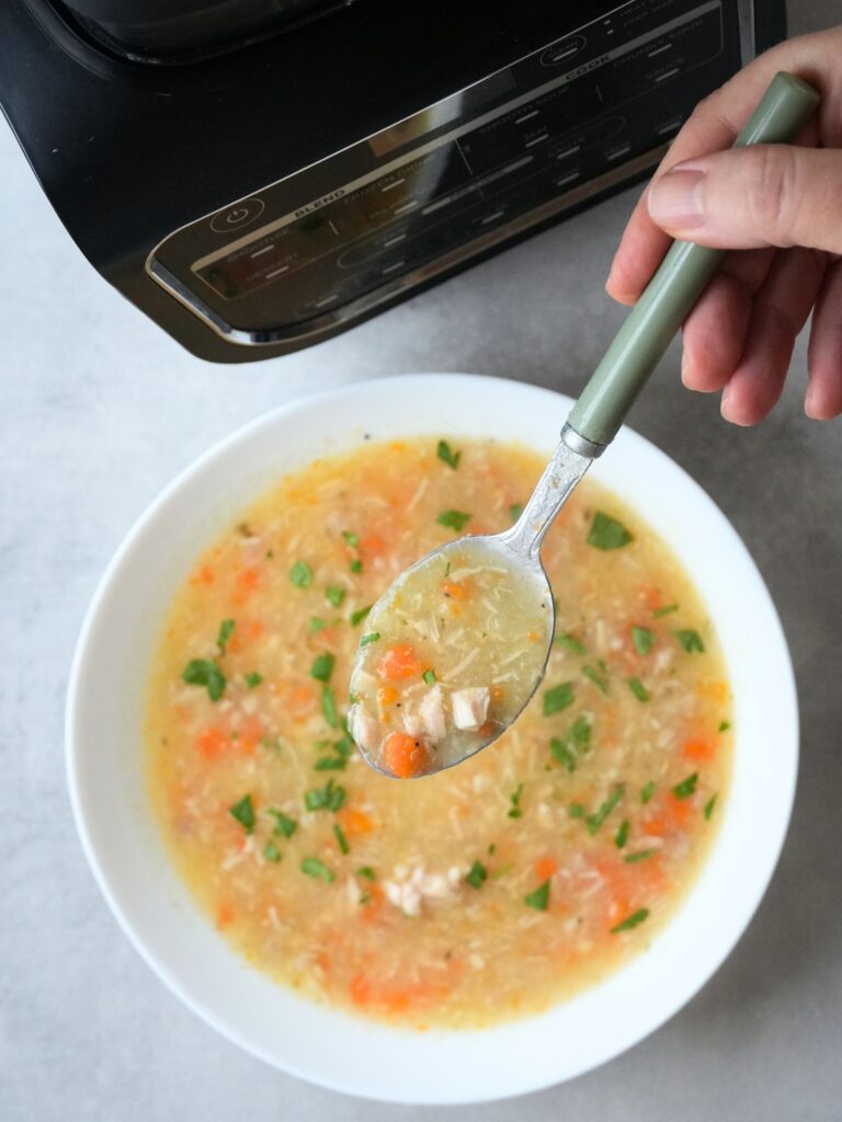 chicken and potato soup in a bowl with carrots and fresh parsley with a spoon held above it