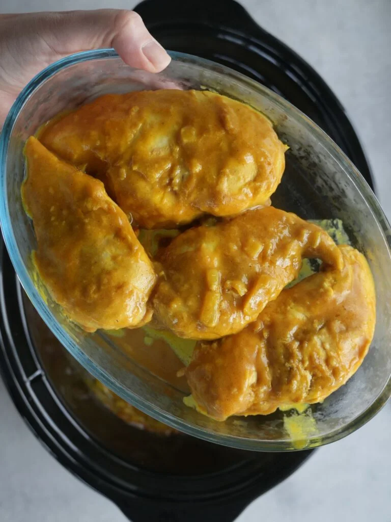 4 cooked chicken breasts covered in Chinese curry sauce in a glass bowl above a slow cooker