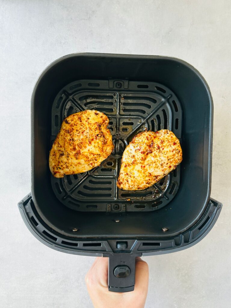 two cooked piri piri chicken breasts in an air fryer basket
