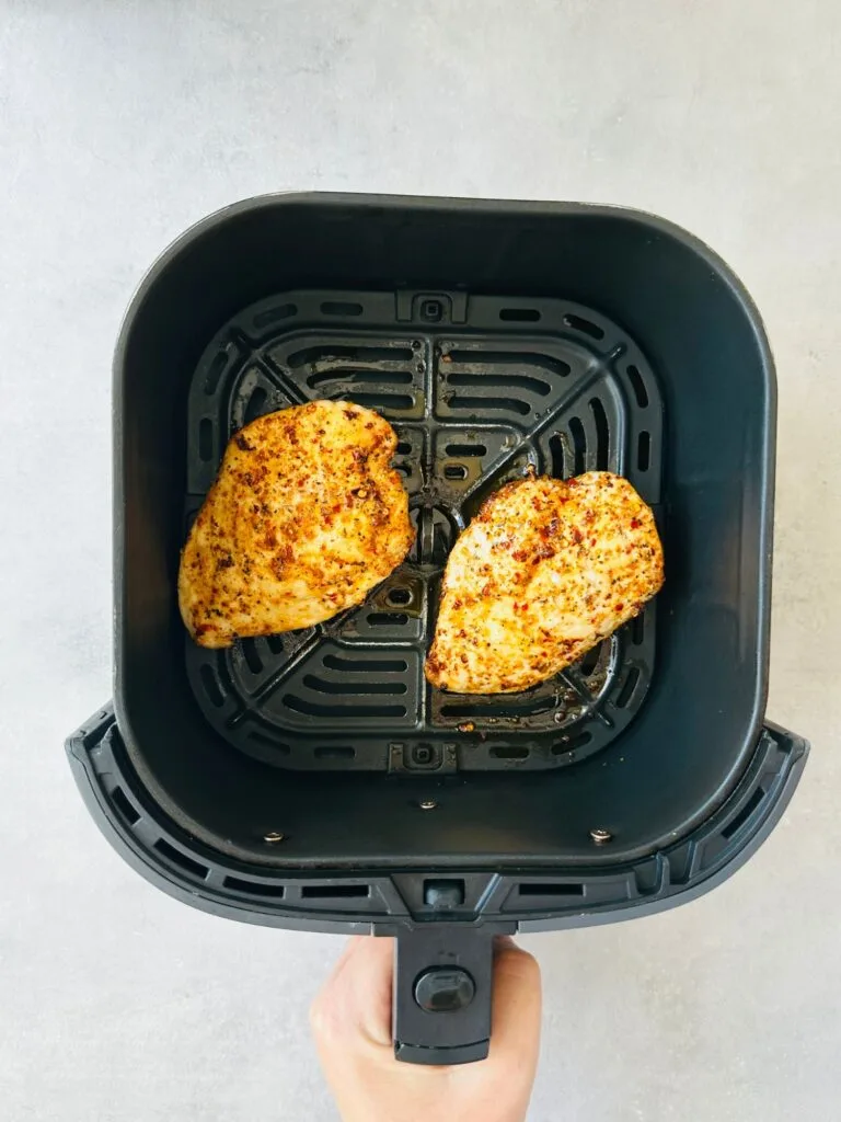 two cooked piri piri chicken breasts in an air fryer basket