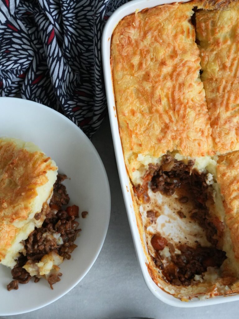 cottage pie in a white oven dish with a portion taken out and put in a serving bowl next to it