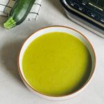 courgette soup in a bowl next to a courgette and Ninja soup maker