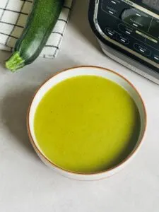 courgette soup in a bowl next to a courgette and Ninja soup maker
