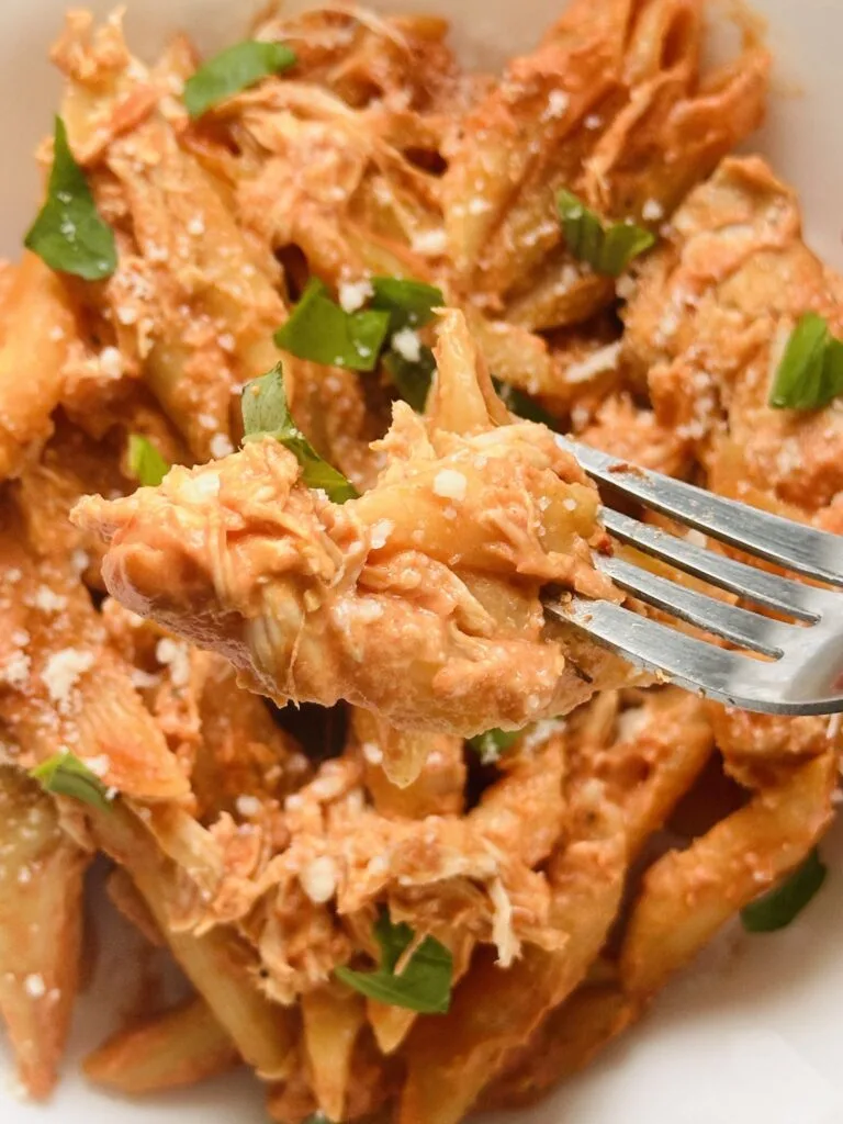 close up of cooked chicken and pasta on a fork with fresh basil leaves and grated parmesan cheese