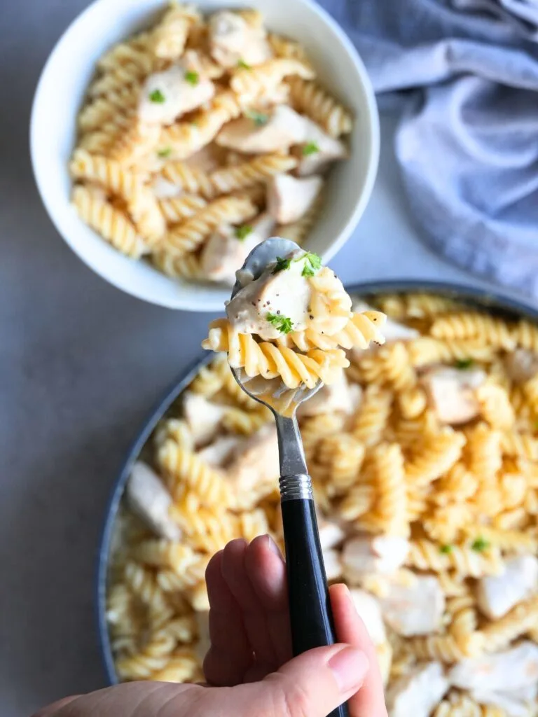 creamy garlic chicken pasta on a spoon above a bowl full of the same food