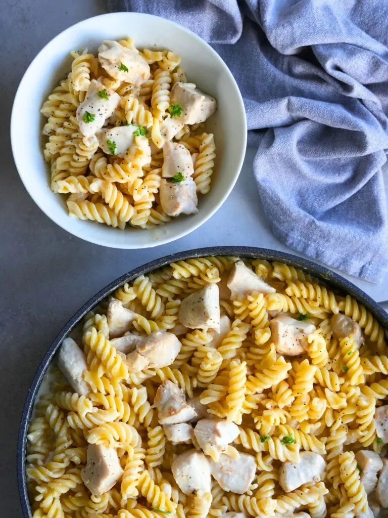 creamy garlic chicken in a pan and a bowl next to a grey tea towel