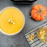 curried pumpkim soup next to a pumpkin and a jar of roasted pumpkin seeds and a Ninja soup maker