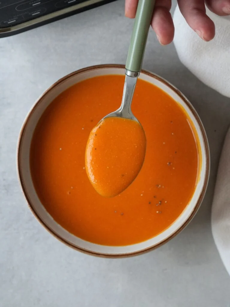curried lentil soup in a bowl with a spoon above it next to a Ninja soup maker