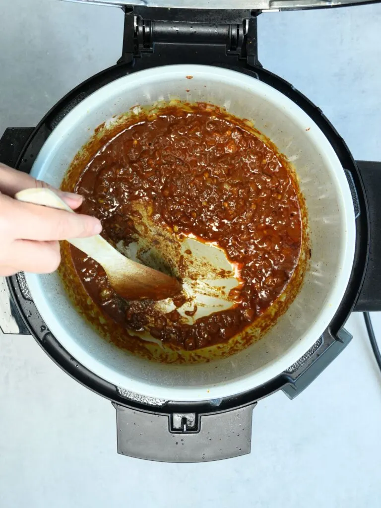 deglazing the Ninja Foodi pot with a wood spatula style spoon