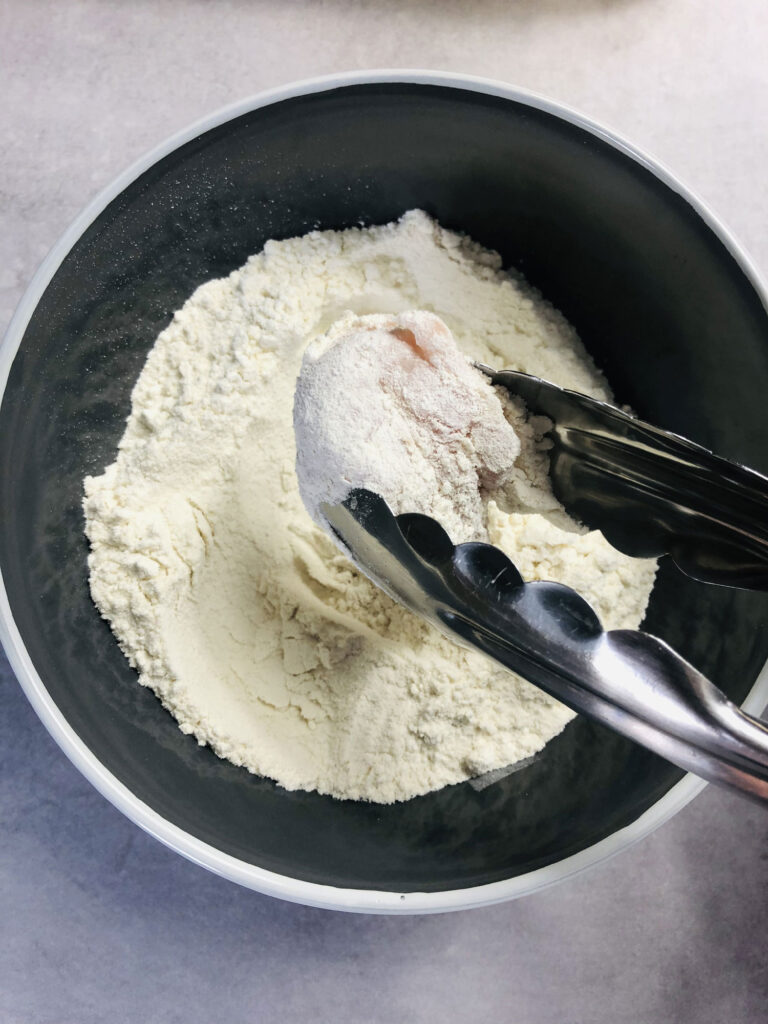 dipping raw chopped chicken in flour with tongs