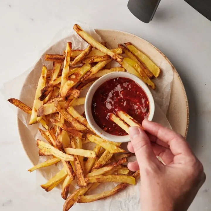 chips being dipped in sauce next to an air fryer