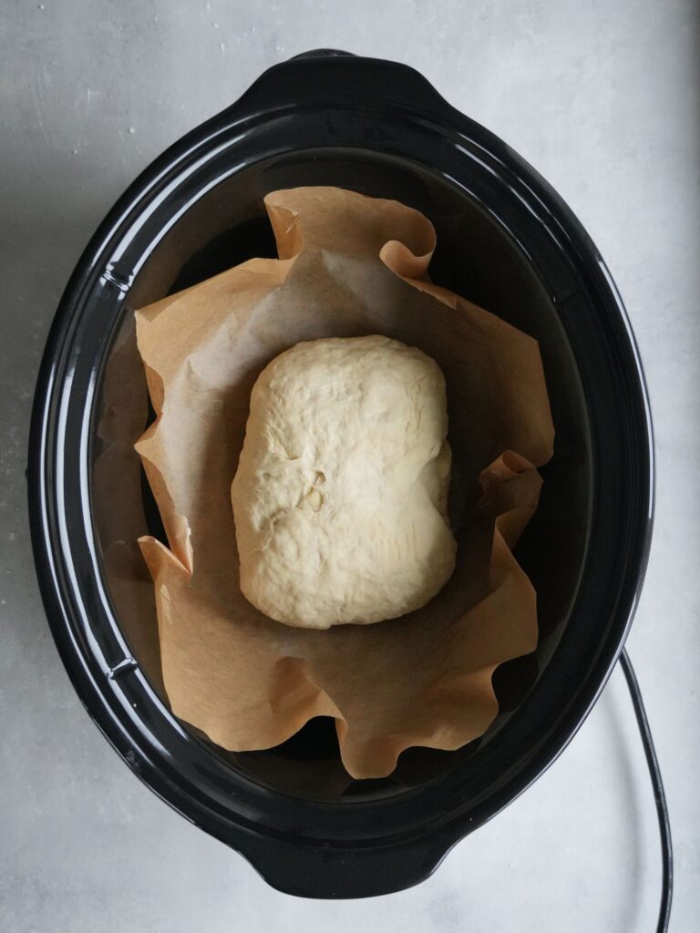 bread dough in a slow cooker on some greaseproof paper getting ready to be cooked