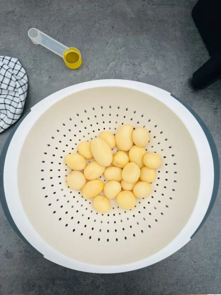 drained tinned potatoes in white colander next to olive oil and air fryer