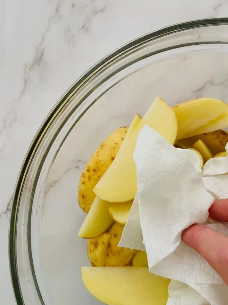 drying off rinsed potato wedges with kitchen roll before putting them in the air fryer basket