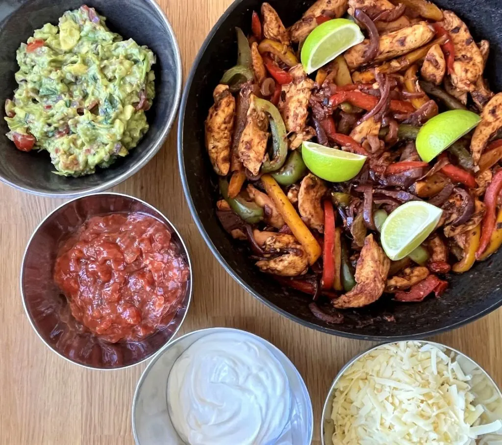 chicken fajitas with guacamole, salsa, sour cream and grated cheese