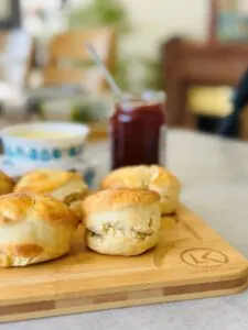 baked scones resting on a wooden chopping board with jam and cream in the background