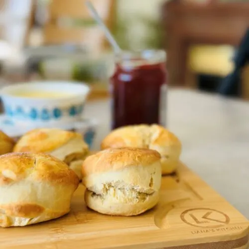 baked scones resting on a wooden chopping board with jam and cream in the background