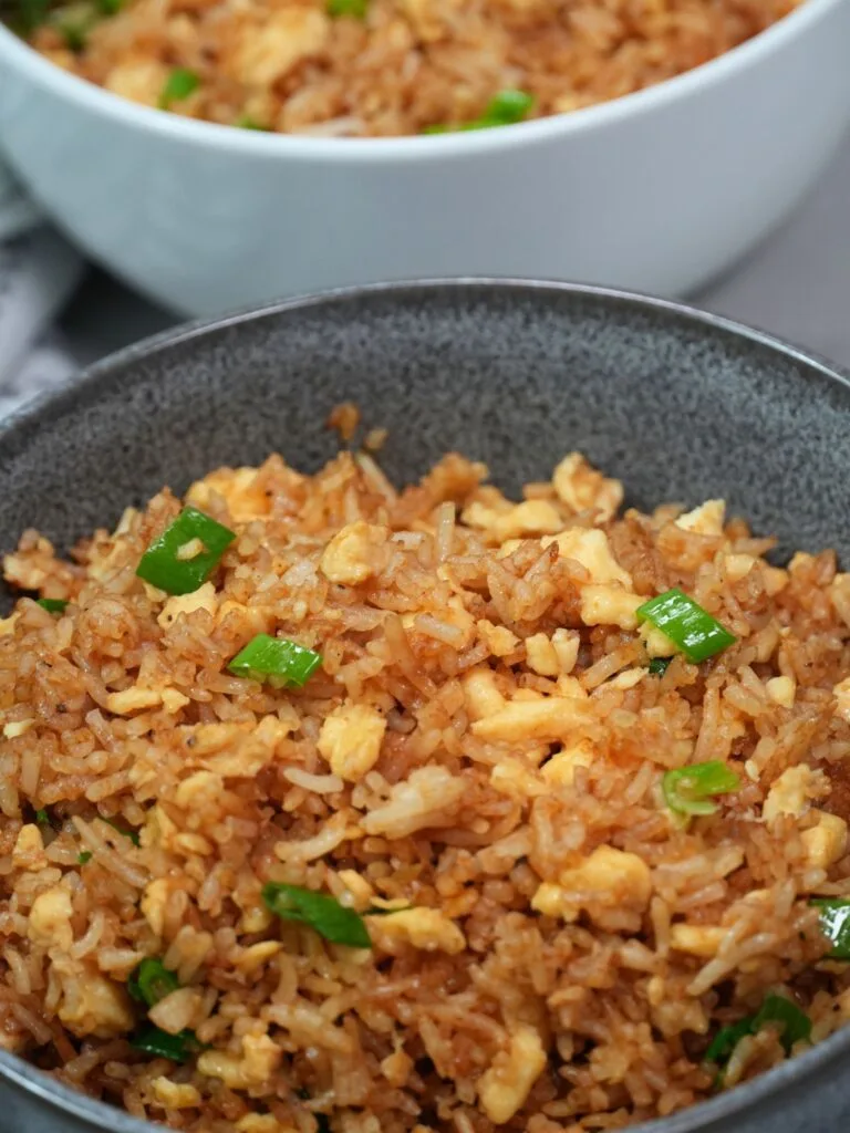 egg fried rice in two seperate bowls with spring onion on top