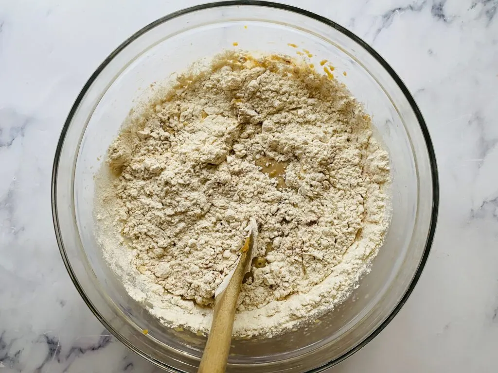 flour with butter sugar eggs and milk in a bowl with wooden mixing spoon