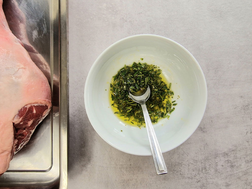 fresh rosemary thyme and garlic in oil next to leg of lamb