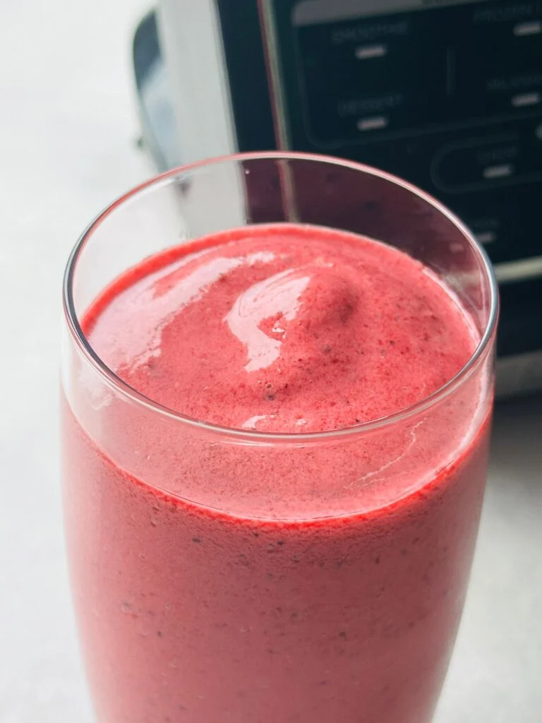 frozen berry smoothie in a glass with the Ninja hot and cold blender sitting behind it