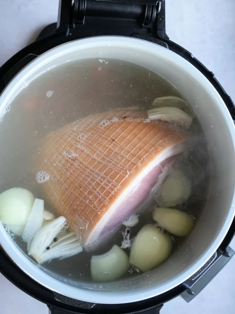 raw gammon in water in a Ninja Foodi 15 in 1 with onions, peppercorns and carrots
