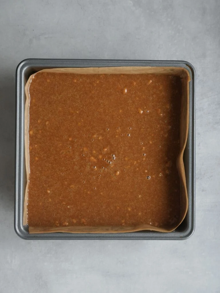 runny batter of ginger cake in a lined square 20cm baking tin ready to go in the oven to be cooked