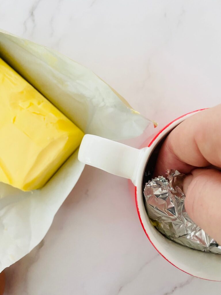 greasing a mug with butter to prepare it for making scrambled egg in the microwave