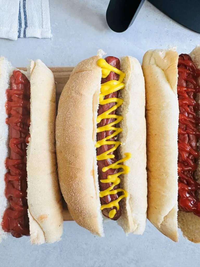 hot dogs with mustard and ketchup lined up next to the air fryer