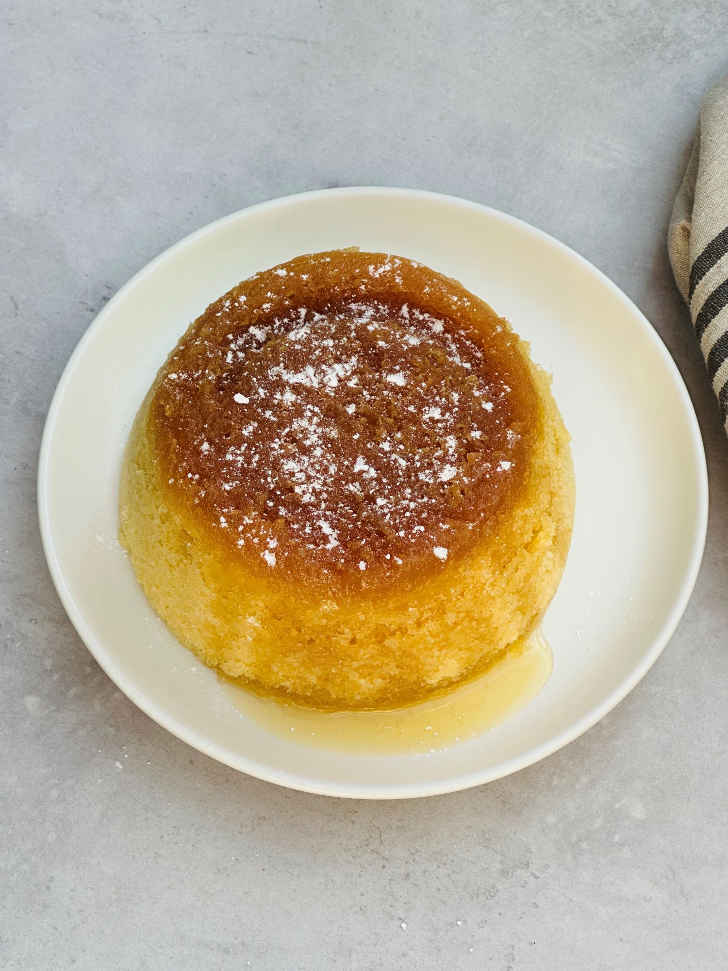 microwave treacle sponge pudding with icing sugar sprinkled on top on a white plate with a tea towel next to it.