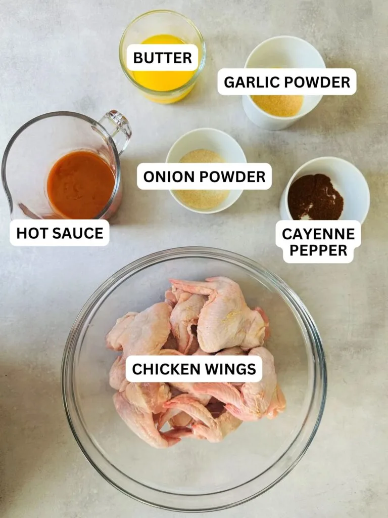 ingredients laid out and labelled for hot chicken wings in the air fryer: melted butter, garlic powder, hot sauce, onion powder, cayenne pepper, chicken wings