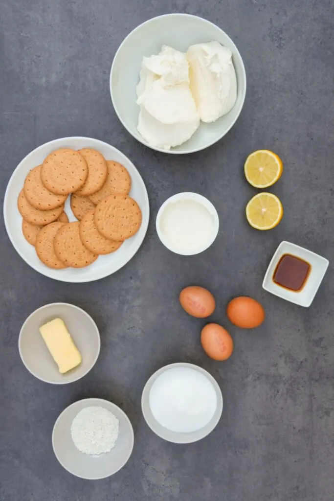 ingredients laid out for air fryer cheesecake: digestive biscuits, cream cheese and sour cream, lemon, vanilla essence, 3 eggs, butter, sugar and flour 