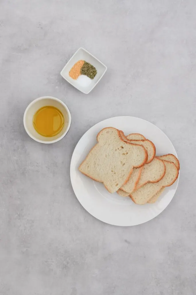 ingredients for air fryer croutons, 5 slices of bread, olive oil and salt, dried herbs and garlic granules in a small bowl