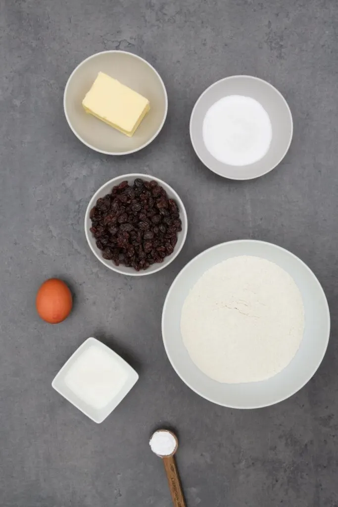 ingredients for air fryer rock cakes: butter, sugar, raisins, flour, egg and milk in seperate bowls