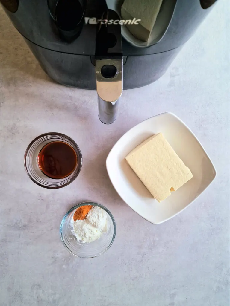 ingredients for air fryer tofu laid out - tofu block, soya sauce, seasoninggs, next to an air fryer