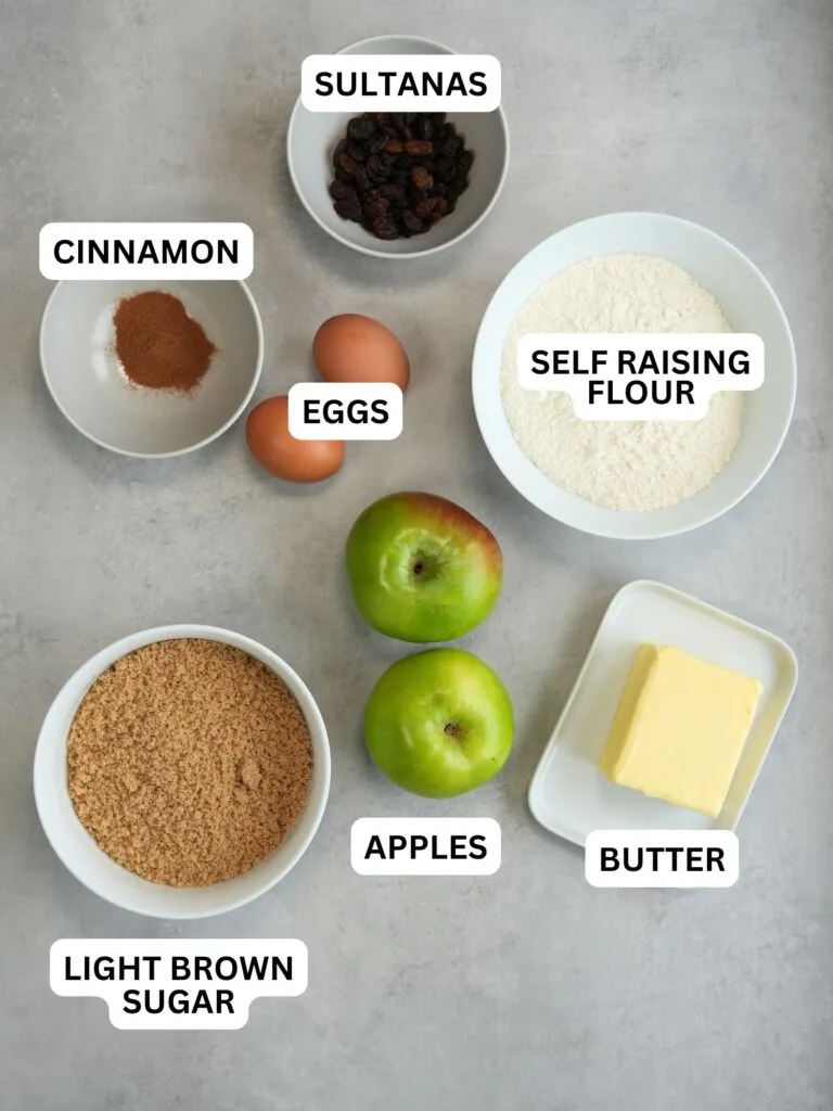ingredients laid out and labelled for apple and cinnamon cake: sultanas, cinnamon, eggs, self raising flour, light brown sugar, apples and butter